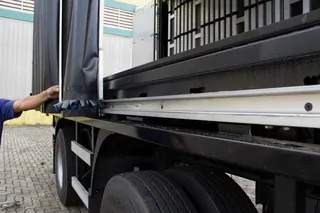 Pessoa abrindo a cortina lateral preta de uma carreta sobre o trilho de alumínio