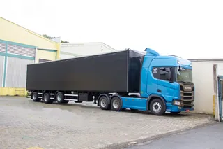 Carreta com lona preta e cavalo mecânico azul estacionados no pátio