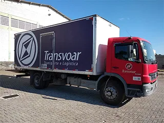Caminhão baú vermelho com lona impressa roxa e a marca Transvoar